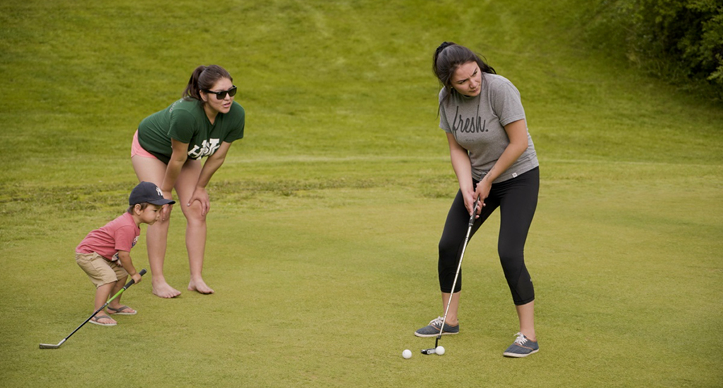 photo of a person putting while two other people watch