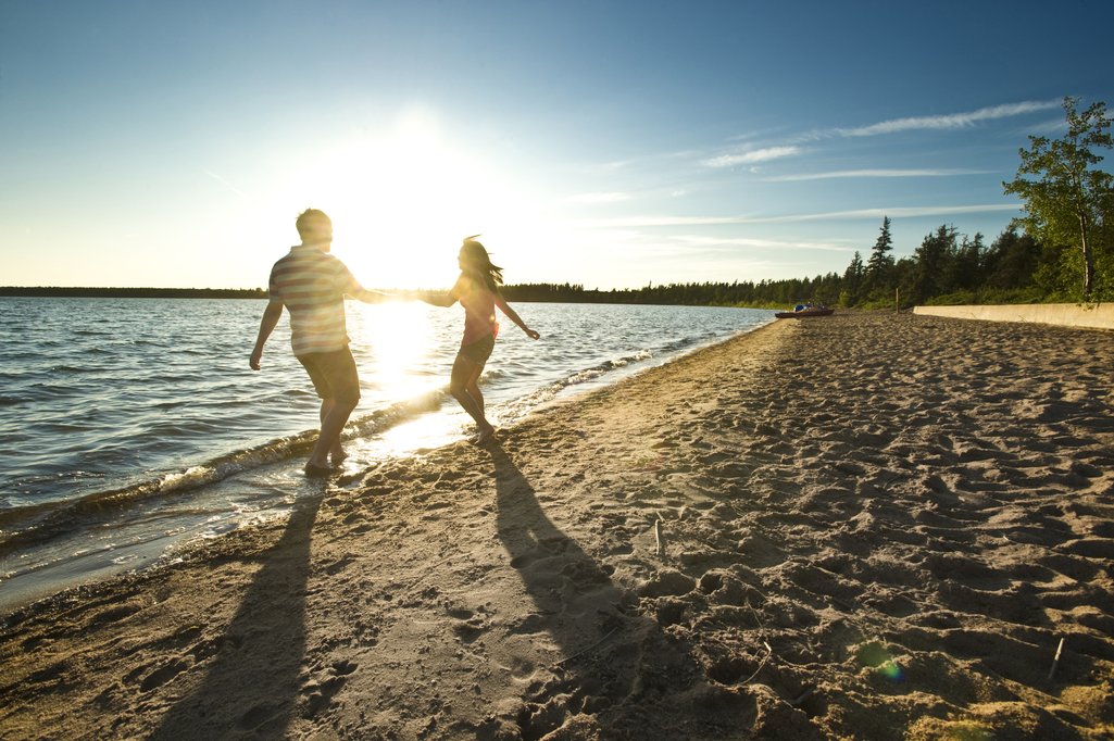 Couple holding hands on beach in Meadow Lake Provincial Park with the sun shining between them