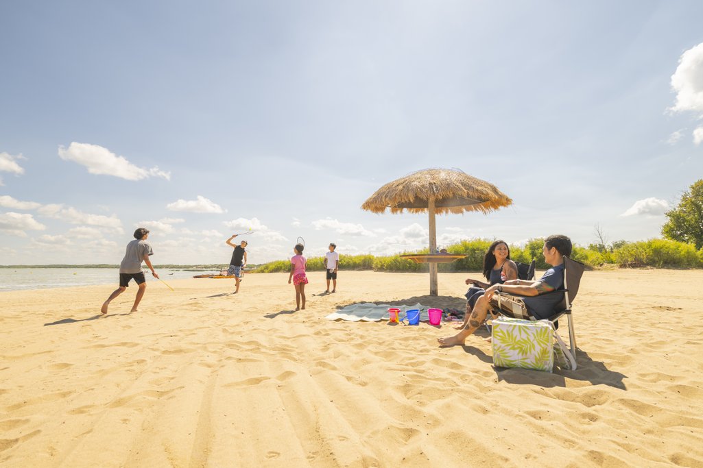 Parents sitting on a beach in lawn chairs beside an umbrella for share while their kids are playing in the sand beside them
