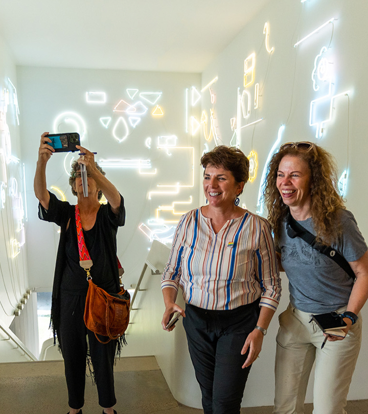 Three happy women in a modern art museum staircase with neon light art on the walls